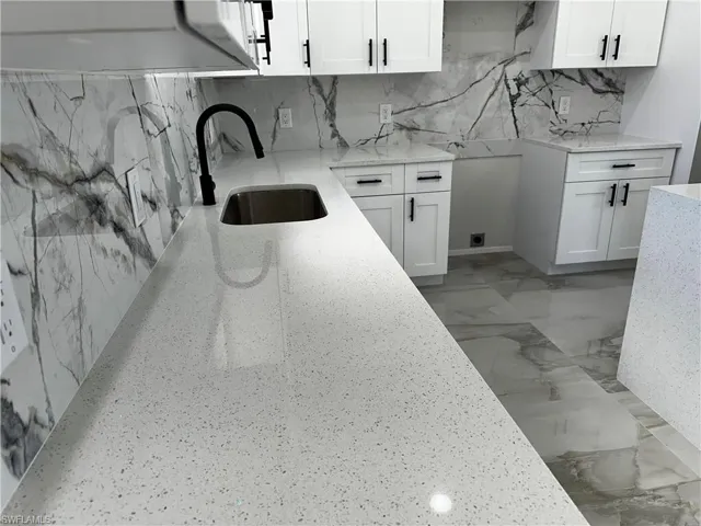 Kitchen featuring backsplash, white cabinetry, sink, and light stone counters