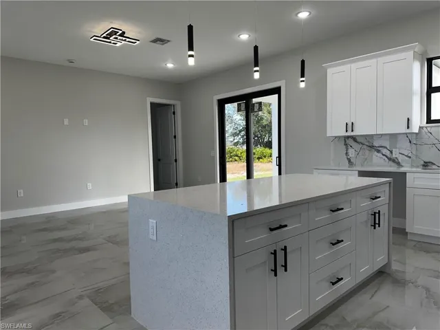 Kitchen featuring pendant lighting, white cabinets, decorative backsplash, a kitchen island, and light stone counters