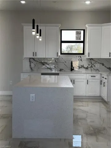 Kitchen with white cabinets, decorative light fixtures, and light stone countertops