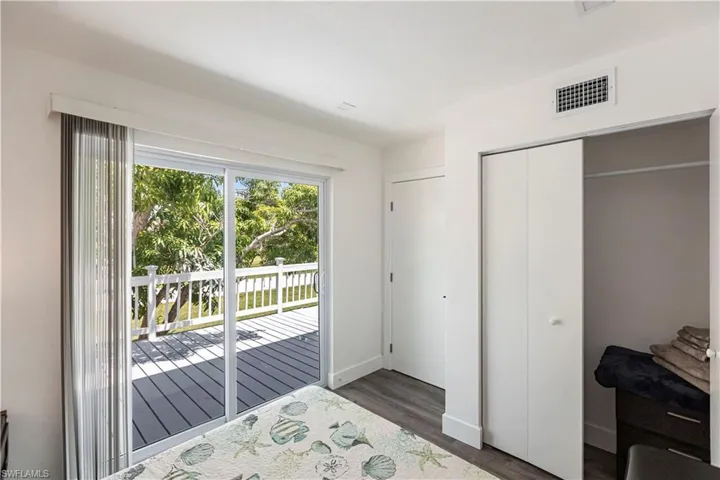 Sliding glass doors opening to an outdoor deck with white railing, featuring wood-finish flooring and a bi-fold closet door