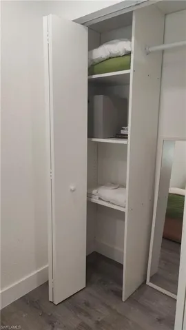 White bifold closet doors opening to built-in shelving, a hanging rod, and wood-finish flooring