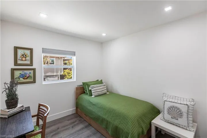 Bright interior room featuring white walls, recessed ceiling lighting, a double-hung window with privacy blinds, and wood-finish flooring