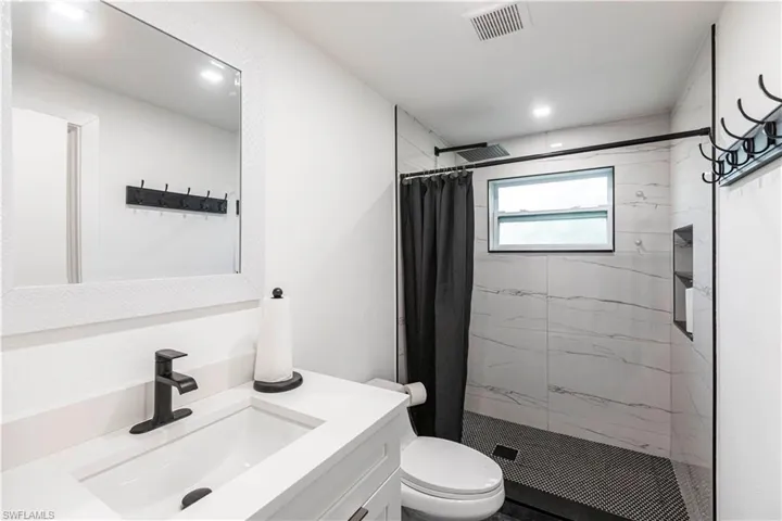Bathroom featuring a single vanity with matte black faucet, a framed mirror, a tiled shower with a window, and recessed shelving