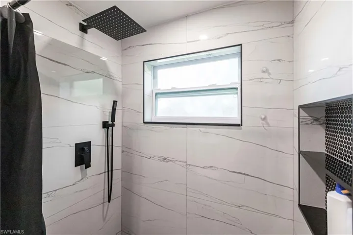 Shower featuring full-height white tile with gray veining, a matte black rainfall showerhead, a matte black handheld shower, and a built-in shower niche with black penny tile backing