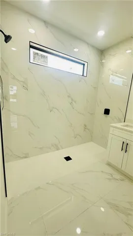 Full bath featuring vanity, a marble finish shower, recessed lighting, and stone wall