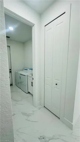 Laundry room with light marble finish flooring and washing machine and clothes dryer