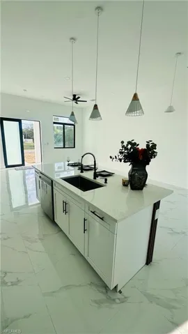 Kitchen with pendant lighting, a kitchen island with sink, light stone counters, white cabinetry, and dishwasher
