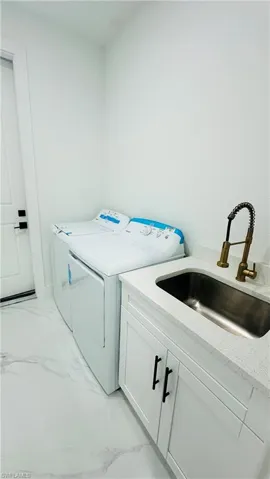 Laundry area featuring washer and clothes dryer, cabinet space, and light marble finish flooring