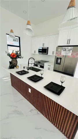 Kitchen with stainless steel appliances, white cabinets, a breakfast bar area, light stone counters, and hanging light fixtures