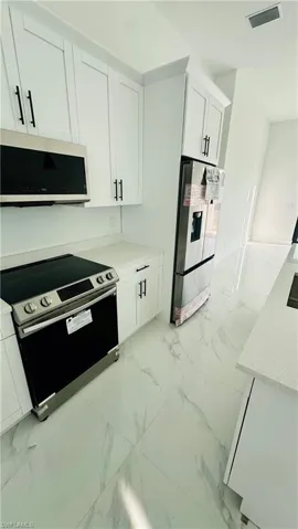 Kitchen with stainless steel appliances, white cabinetry, light marble finish floors, and light stone countertops