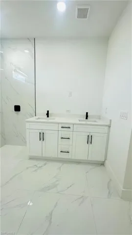 Bathroom with double vanity, light marble finish flooring, and recessed lighting