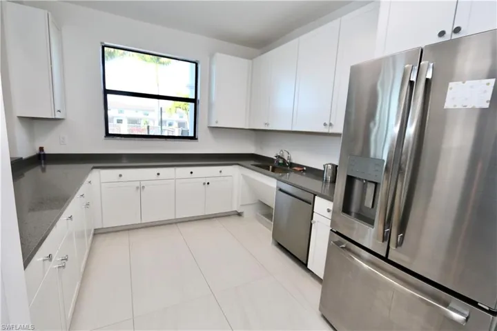 Kitchen featuring appliances with stainless steel finishes, white cabinets, light tile patterned flooring, and dark stone countertops