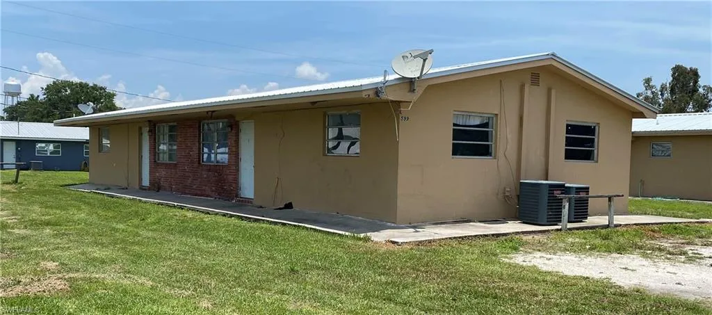 Rear view of property with a lawn, metal roof, cooling unit, and stucco siding