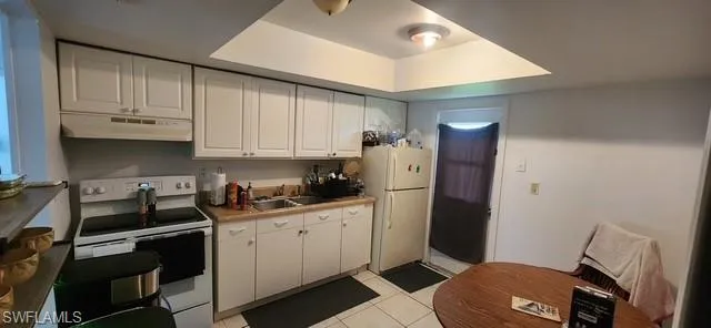Kitchen featuring white appliances, white cabinets, under cabinet range hood, and light tile patterned flooring