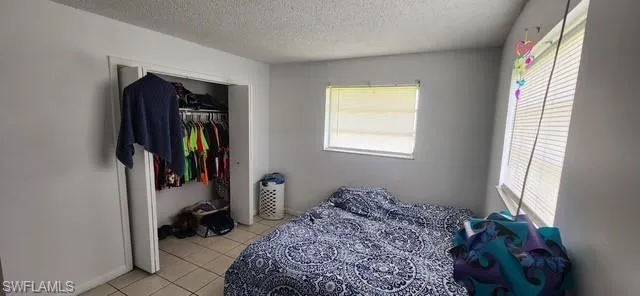 Bedroom featuring multiple windows, a textured ceiling, light tile patterned floors, and a closet