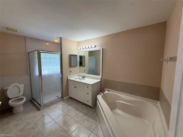 Full bath with vanity, toilet, a shower stall, a bath, and a textured ceiling
