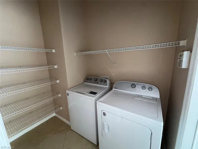 Laundry room featuring washer and dryer, light tile patterned flooring, and baseboards