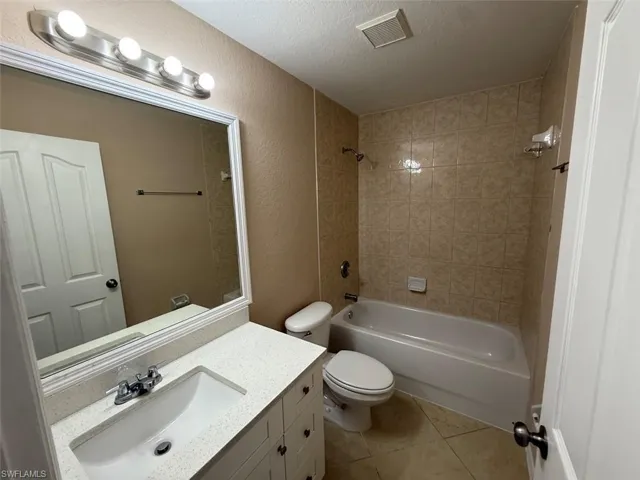 Full bathroom with vanity, tile patterned flooring, toilet, bathing tub / shower combination, and a textured ceiling