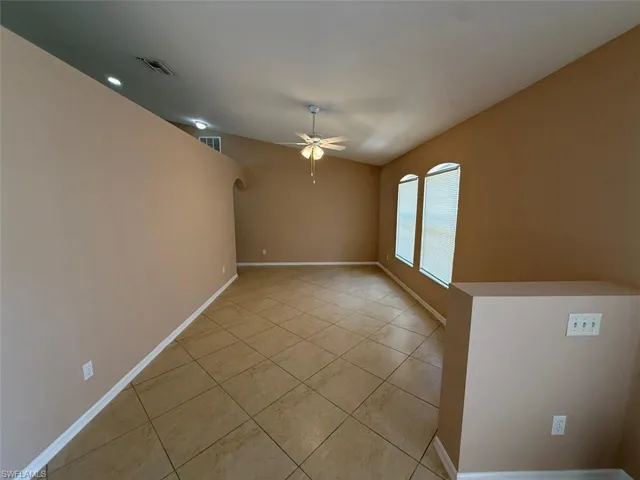 Unfurnished room featuring ceiling fan, light tile patterned floors, baseboards, and arched walkways