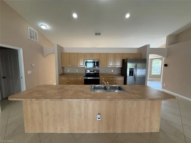 Kitchen with appliances with stainless steel finishes, a sink, arched walkways, light tile patterned floors, and light brown cabinetry