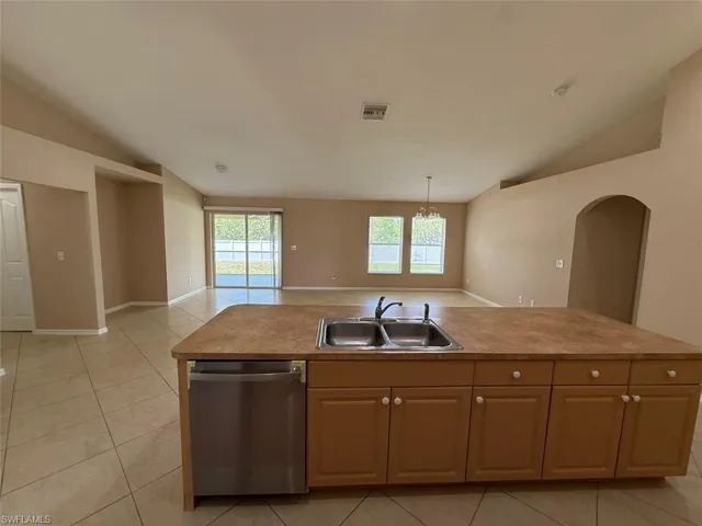 Kitchen featuring stainless steel dishwasher, a sink, lofted ceiling, light tile patterned floors, and arched walkways