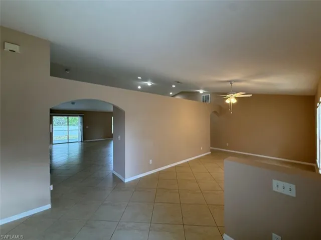 Spare room with arched walkways, light tile patterned flooring, a ceiling fan, baseboards, and lofted ceiling