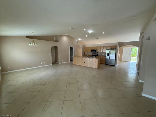 Kitchen with appliances with stainless steel finishes, open floor plan, arched walkways, vaulted ceiling, and baseboards