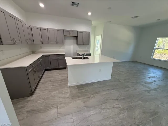 Kitchen with gray cabinets, a kitchen island with sink, light stone counters, and recessed lighting