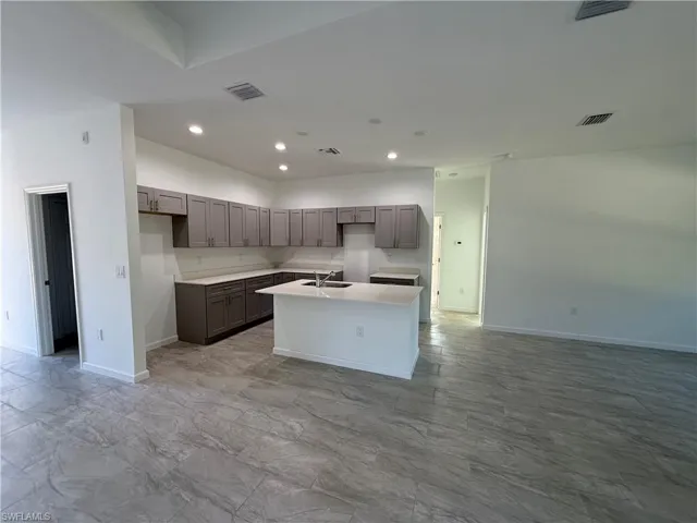 Kitchen featuring a kitchen island with sink, gray cabinetry, recessed lighting, open floor plan, and light stone countertops