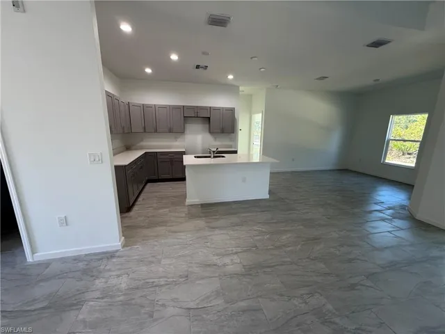 Kitchen with recessed lighting, an island with sink, open floor plan, light stone counters, and gray cabinetry