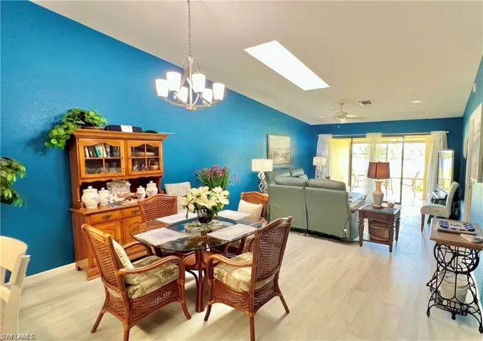 Dining area featuring ceiling fan with notable chandelier, vaulted ceiling with skylight, and light wood-type flooring