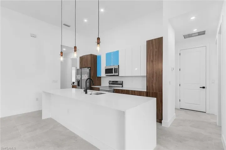 Kitchen featuring pendant lighting, a center island with sink, white cabinets, sink, and stainless steel appliances