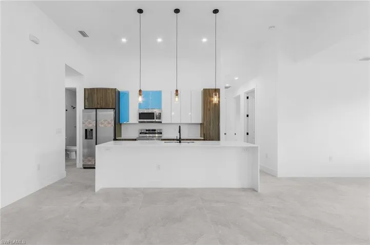 Kitchen with a kitchen island with sink, hanging light fixtures, white cabinets, and stainless steel appliances