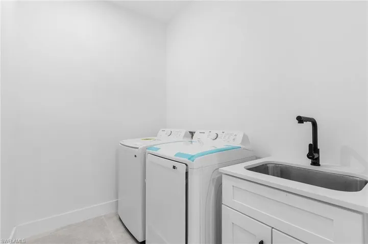 Laundry area featuring washer and clothes dryer, light tile patterned floors, cabinets, and sink