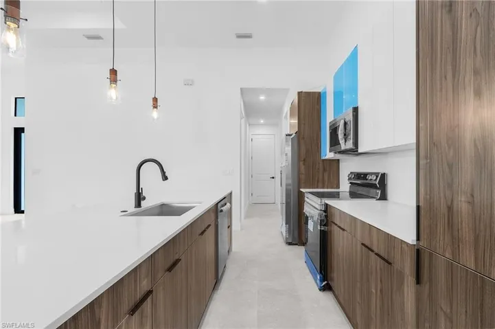 Kitchen featuring white cabinets, appliances with stainless steel finishes, decorative light fixtures, and sink