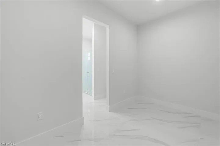 Bright interior room featuring white walls, white baseboards, and large-format tile flooring with a subtle veined pattern