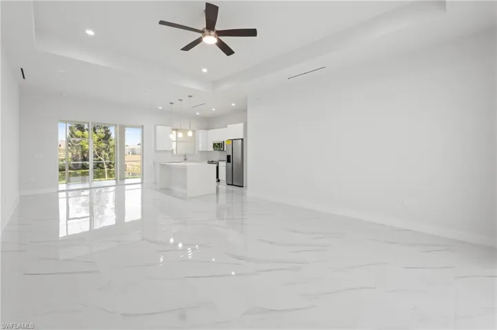 Expansive open concept living area featuring large format white tile flooring with subtle veining, a tray ceiling with recessed lighting, and a contemporary ceiling fan