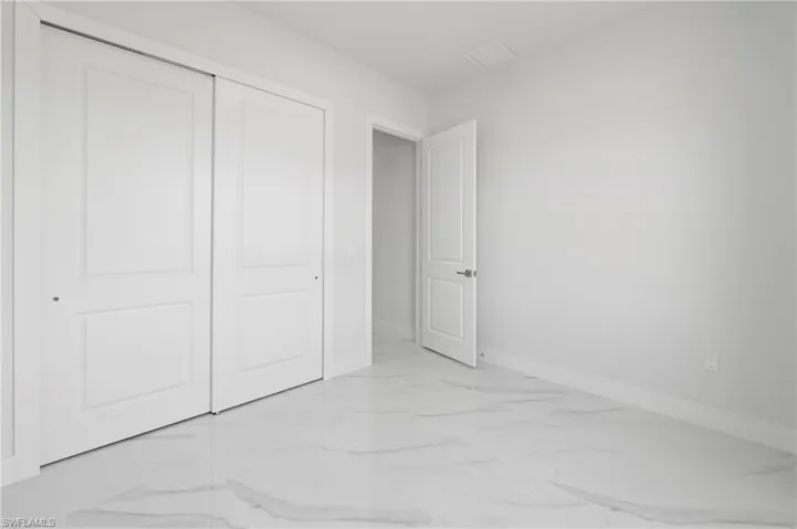 Room featuring white walls, matching baseboards, and bright white tile flooring with subtle gray veining