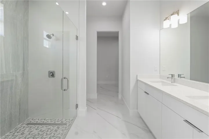 Spacious bathroom featuring a frameless glass shower enclosure, a dual vanity with a light-toned countertop, and modern chrome fixtures