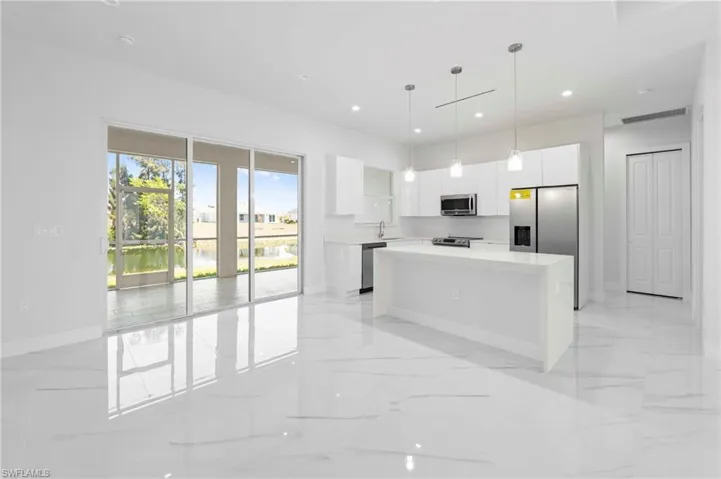 Modern kitchen featuring an expansive island, white cabinetry, stainless steel appliances, and sleek pendant lighting