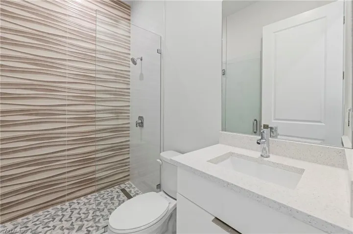 Contemporary bathroom with a frameless glass shower enclosure, a vanity featuring a white integrated sink and speckled countertop, and a large wall-mounted mirror
