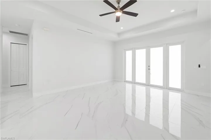 Spacious room with polished tile flooring, tray ceiling, recessed lighting, and a ceiling fan