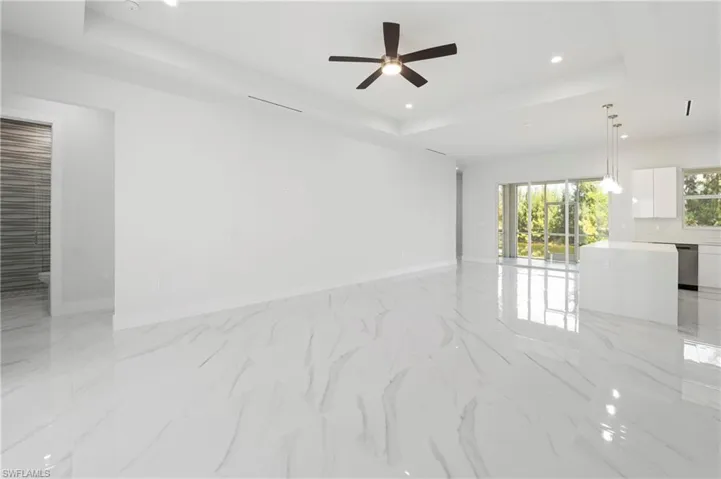 Spacious open-concept living area featuring large format polished tile flooring, a tray ceiling, and a ceiling fan with integrated lighting