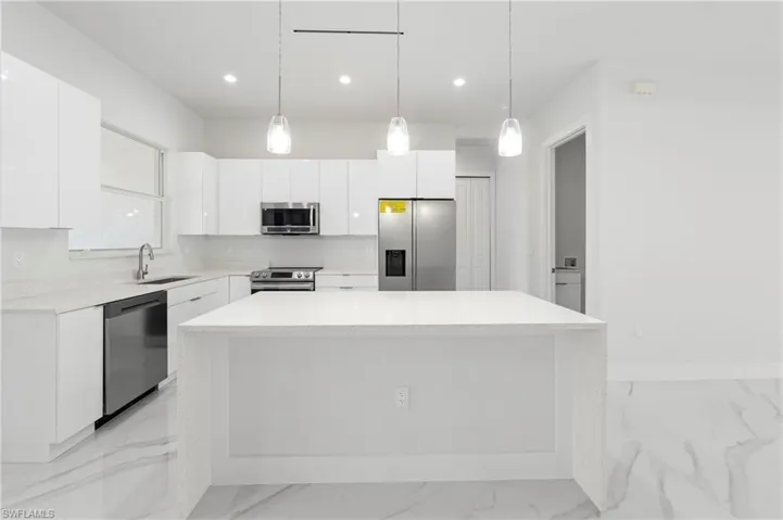 Contemporary kitchen featuring a substantial central island with pendant lighting, white cabinetry, integrated stainless steel appliances, and sleek stone countertops