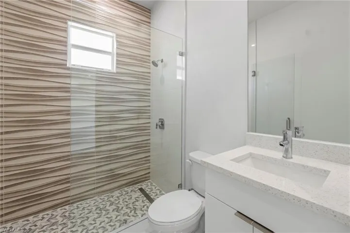 Contemporary bathroom featuring a floating vanity with a white countertop and integrated sink, a frameless mirror, and a glass-enclosed shower with textured wall tile and patterned floor tile