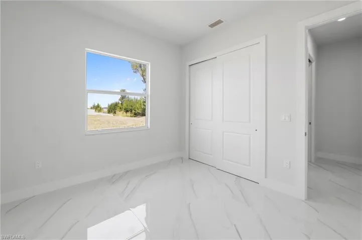 Room featuring large format white tile flooring with gray veining, a white-framed window, and a white sliding closet door