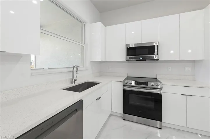 Modern kitchen featuring white high-gloss cabinetry, light-toned countertops, a stainless steel range, and an integrated stainless steel microwave