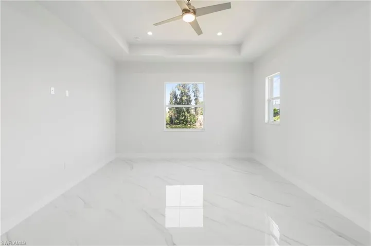Spacious room featuring large format tile flooring, a tray ceiling, recessed lighting, and a ceiling fan
