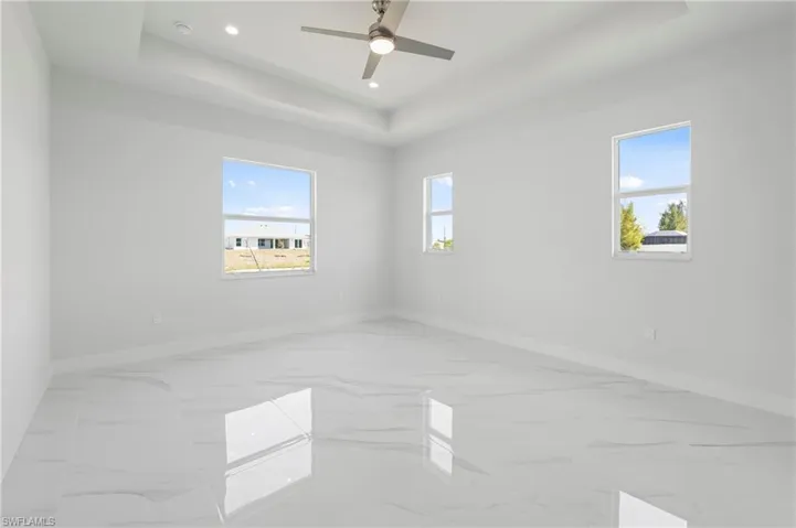 Spacious room featuring large format tile flooring, a tray ceiling with recessed lighting, and a modern ceiling fan