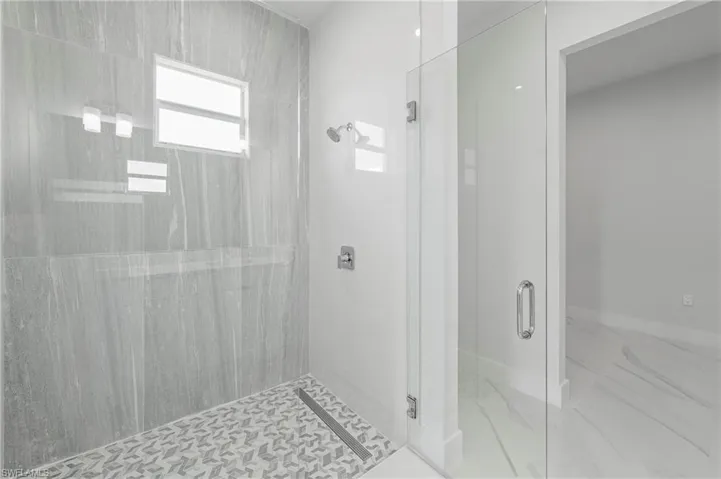 Spacious shower enclosure featuring full-height gray wall tiling, a patterned floor, and a linear drain